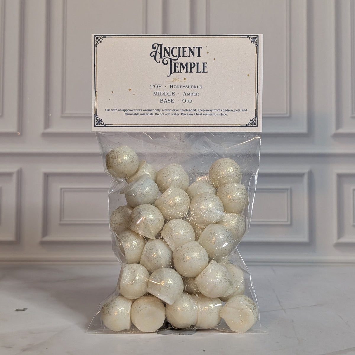 Ancient Temple wax melt drops in a sealed cello bag with a navy and gold topper card, on white marble