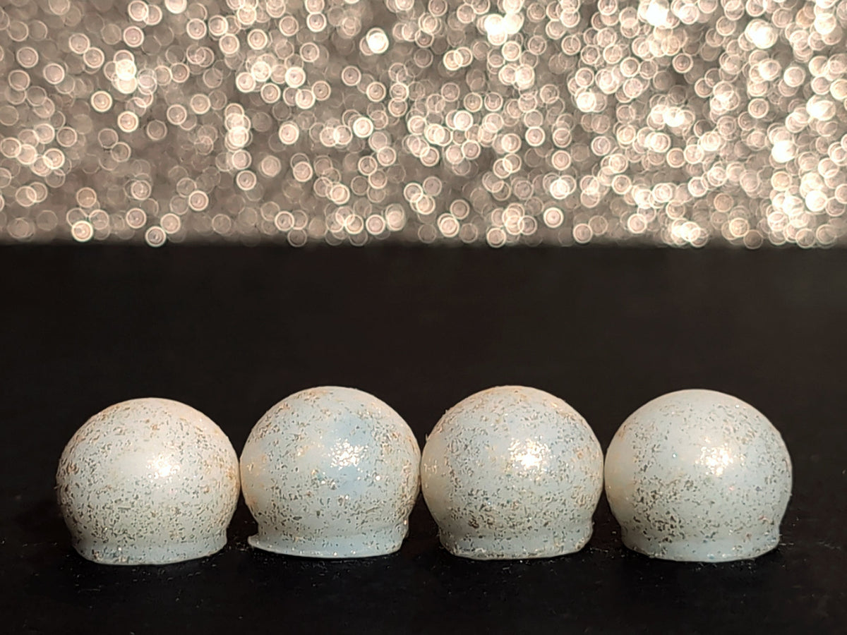 Four Ancient Temple wax melt drops on a dark surface, showing the cream wax and brilliant gold mica