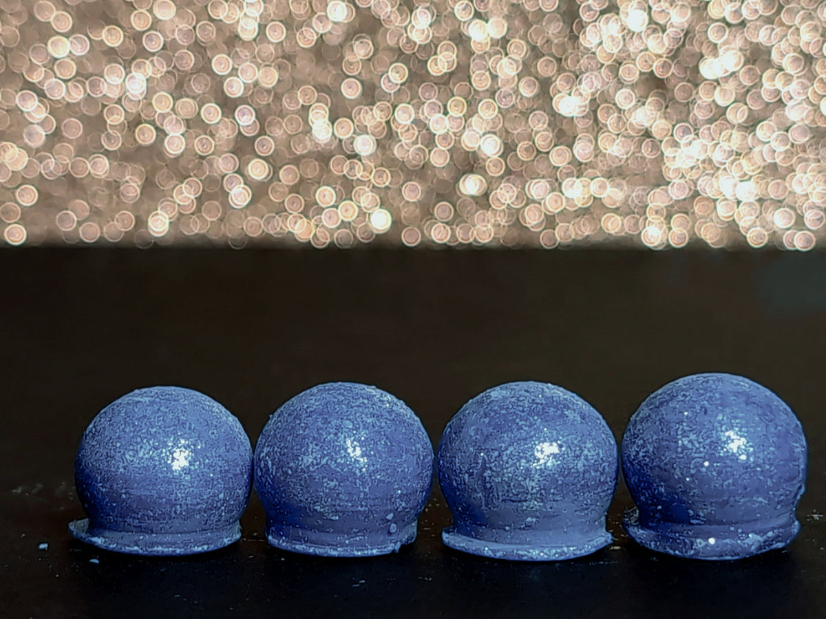 Four Deliciously Dusted Blueberry Cupcake wax melt drops on a dark surface, showing the blue wax and sparkling silver mica
