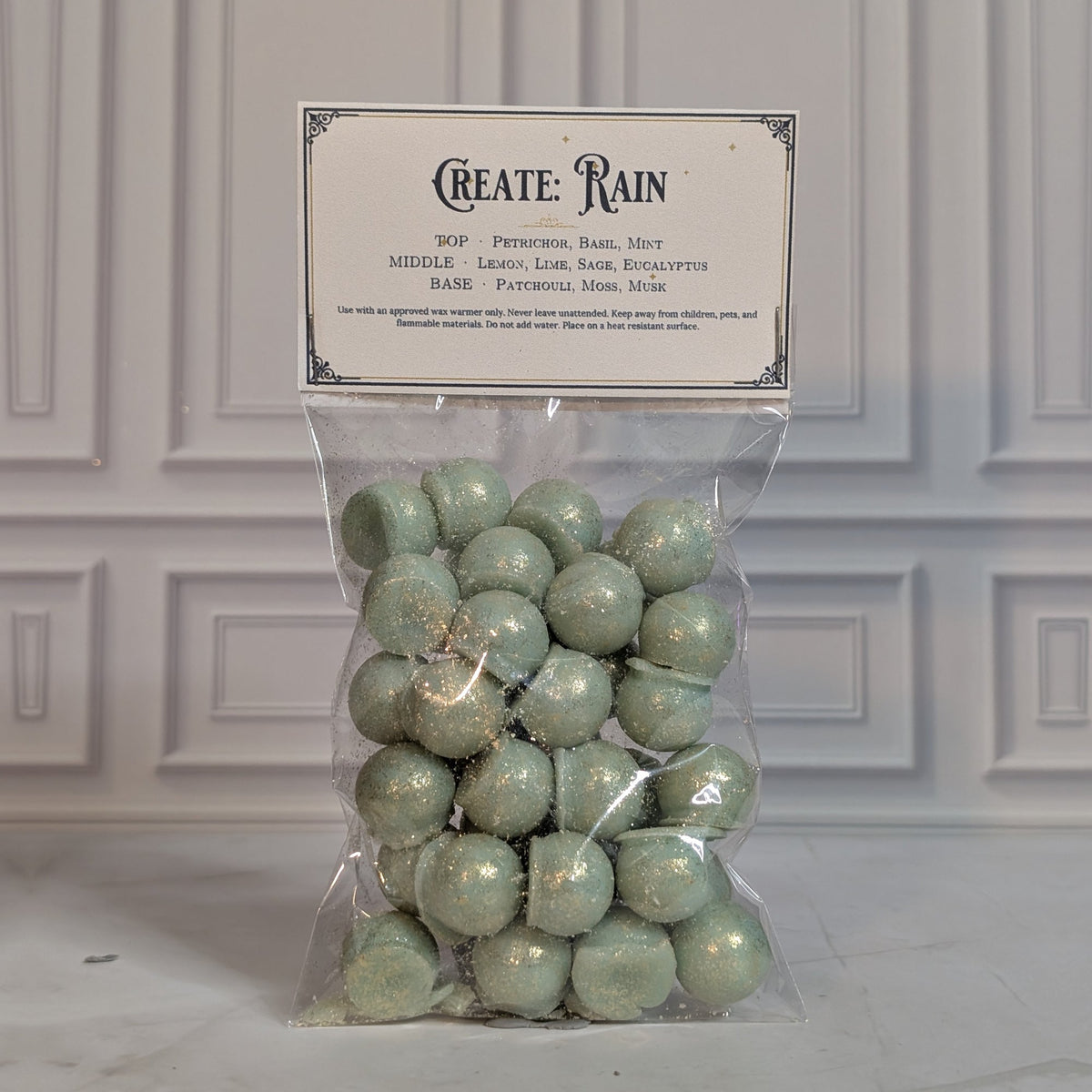 Create: Rain wax melt drops in a sealed cello bag with a navy and gold topper card, on white marble