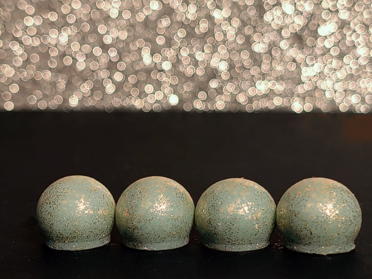 Four Create: Rain wax melt drops on a dark surface, showing the pale sage wax and brilliant gold mica