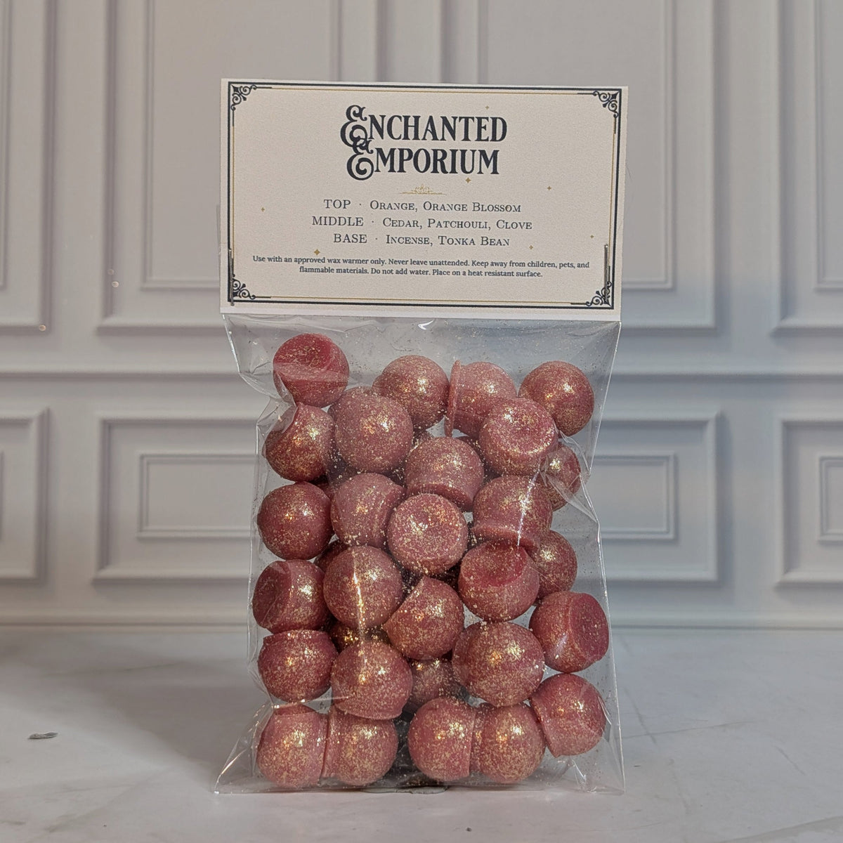 Enchanted Emporium wax melt drops in a sealed cello bag with a navy and gold topper card, on white marble