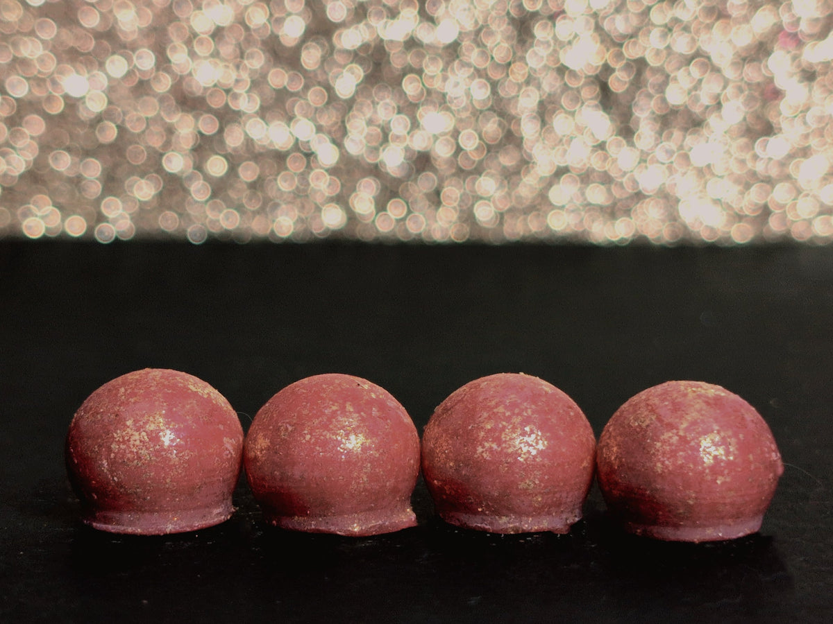 Four Enchanted Emporium wax melt drops on a dark surface, showing the rose madder wax and brilliant gold mica