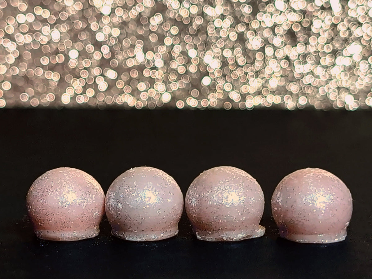 Four Goodberry wax melt drops on a dark surface, showing the pink wax and sparkling silver mica