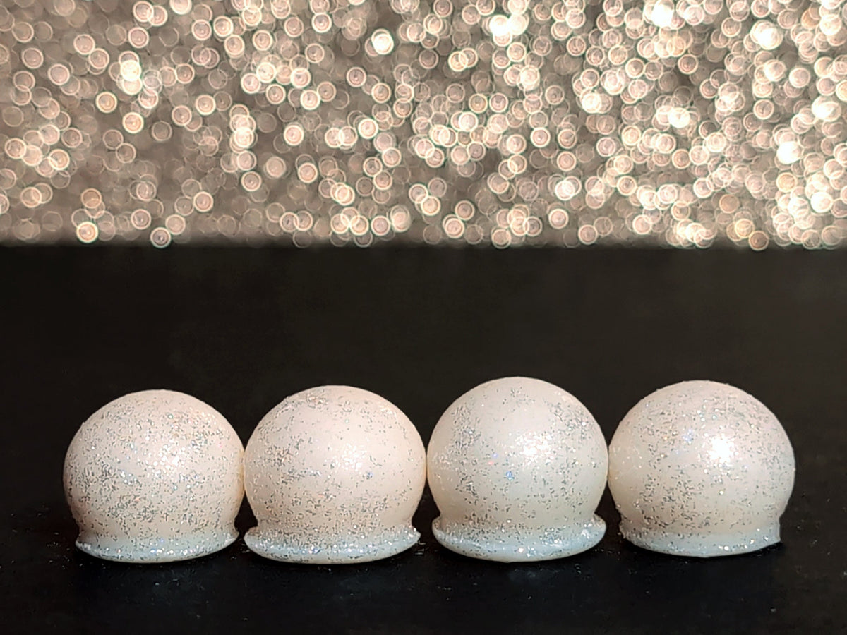Four Prestidigitation wax melt drops on a dark surface, showing the white wax and sparkling silver mica