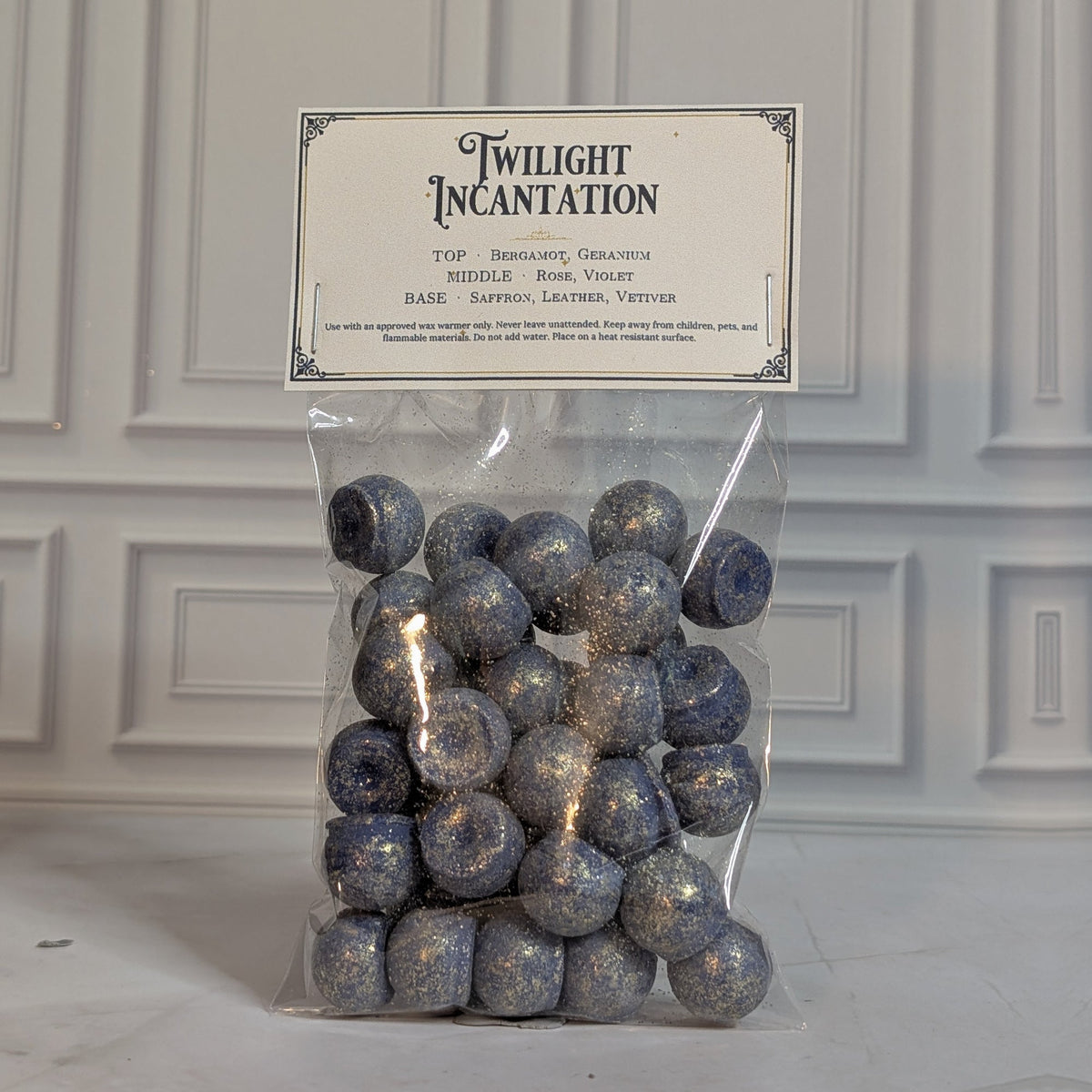 Twilight Incantation wax melt drops in a sealed cello bag with a navy and gold topper card, on white marble