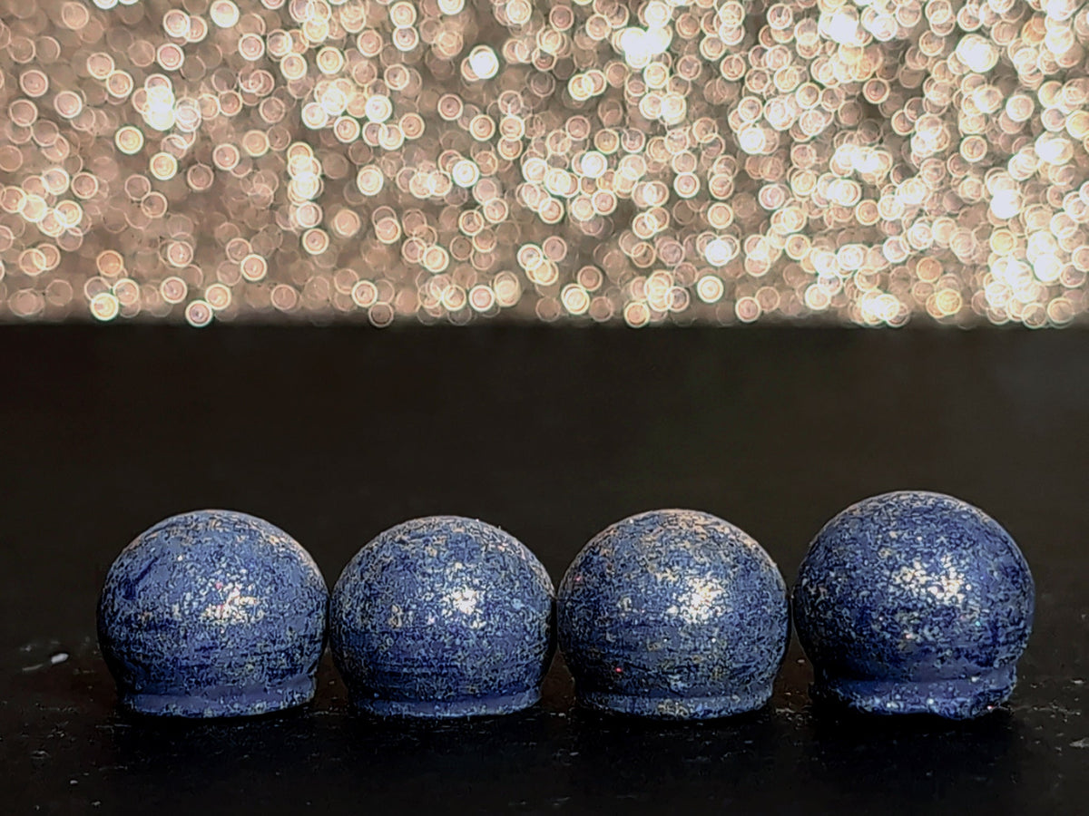 Four Twilight Incantation wax melt drops on a dark surface, showing the periwinkle wax and brilliant gold mica