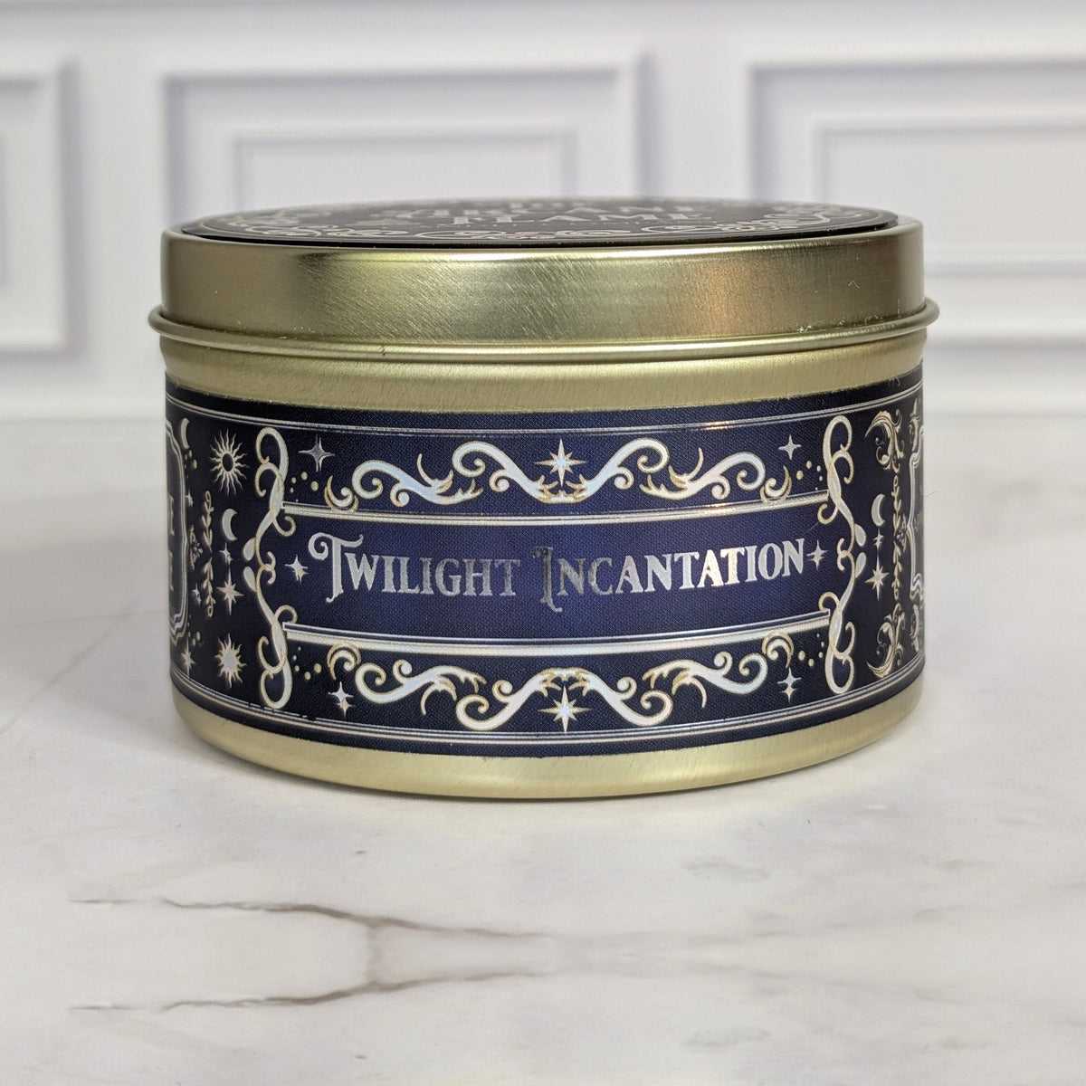 Twilight Incantation 8oz soy candle in a gold tin with a navy and gold foil label, on white marble